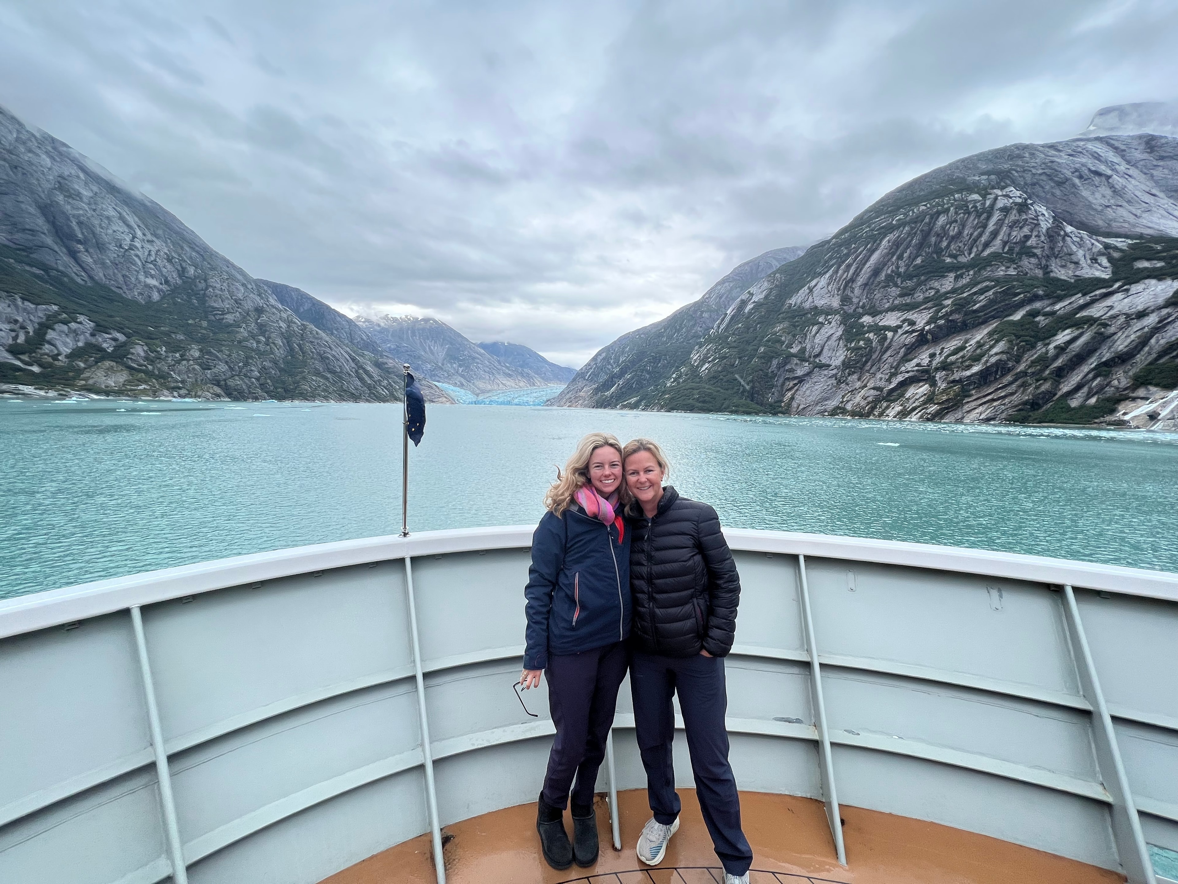 Two travellers on the bow of a ship approaching a glacier fjord