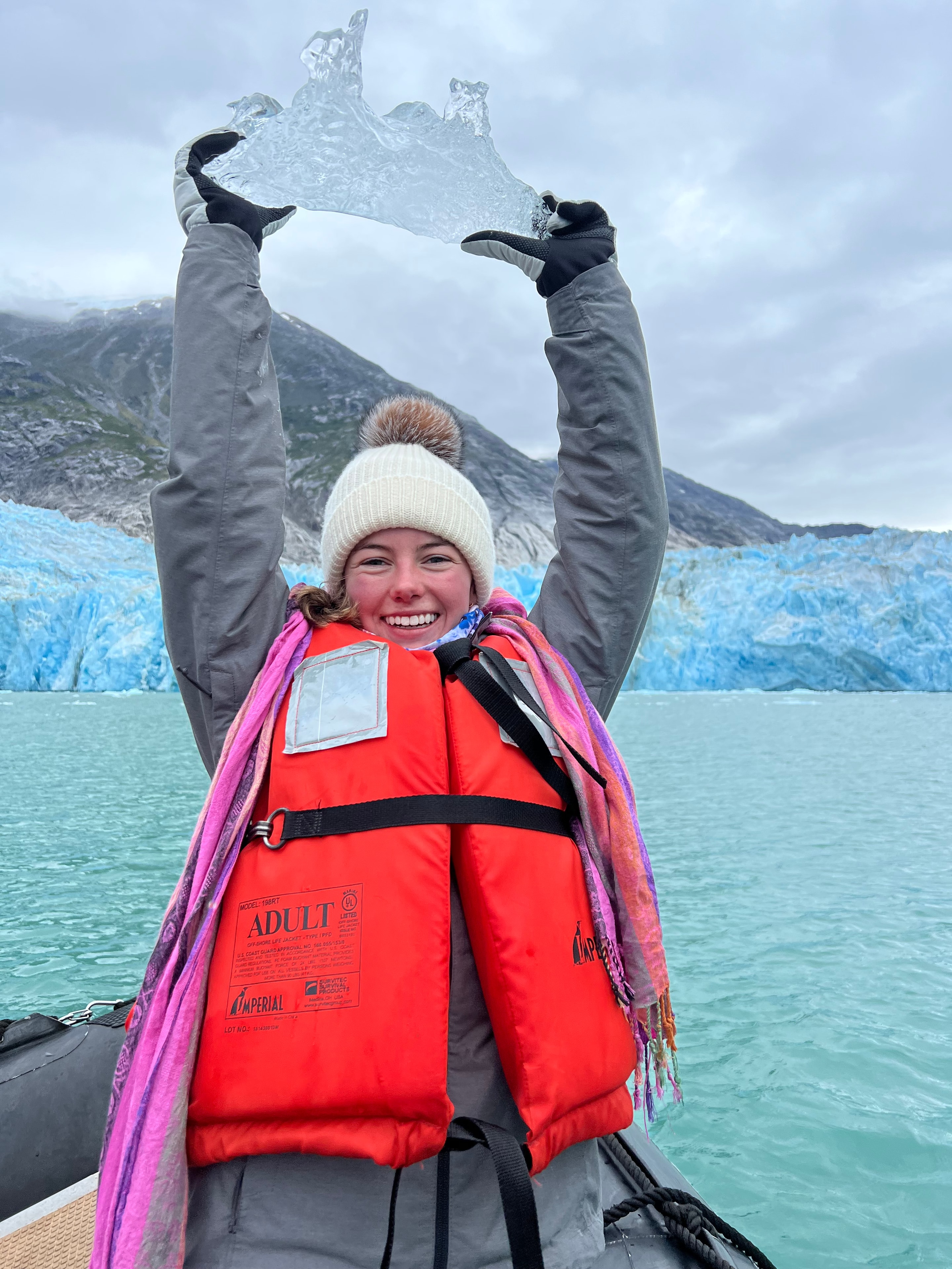 Cindy holding a piece of glacier ice by turquoise water